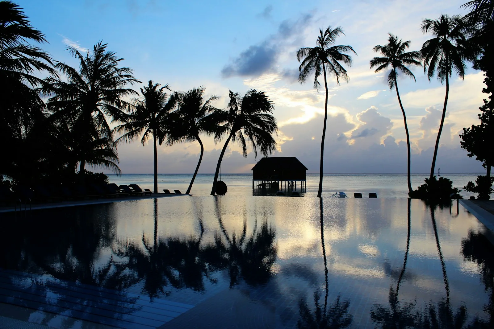 Piscina de um resort nas Maldivas cercada por palmeiras ao pôr do sol